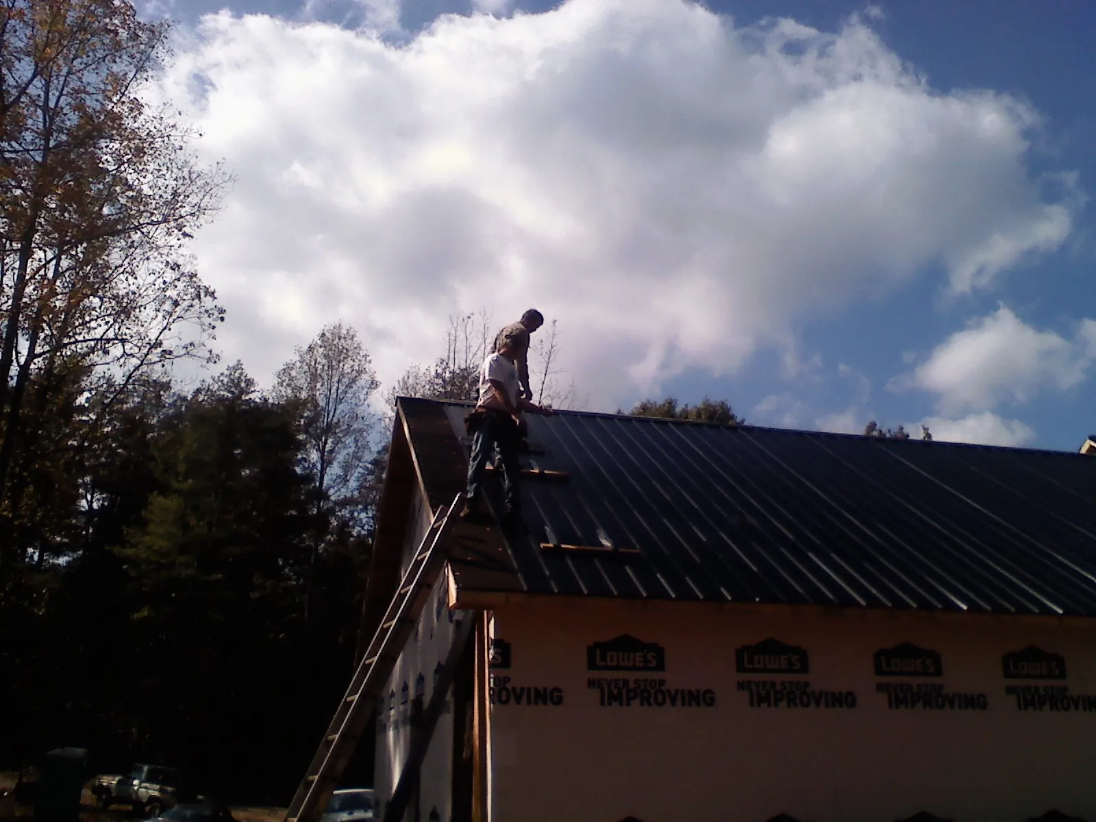 Roofer fastening dark metal panels high against a cloudy sky in Jackson
